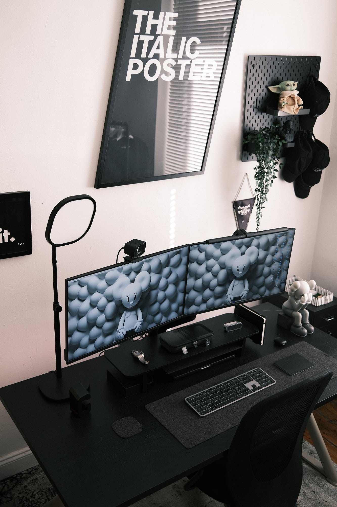 A workspace setup with dual Dell S2721QSA 27″ monitors on an ISY IMA-2100 dual-monitor arm, an Elgato Key Light, a MonsGeek M1 keyboard, and a Grovemade wool felt desk pad on a black desk, with wall decor and a pegboard holding caps and a small Grogu figure